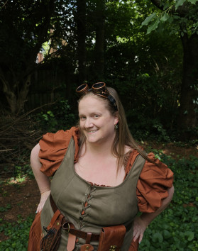 HistoryGal dressed in a mixture of steampunk and medieval attire, standing in a forest-like field in a backyard.